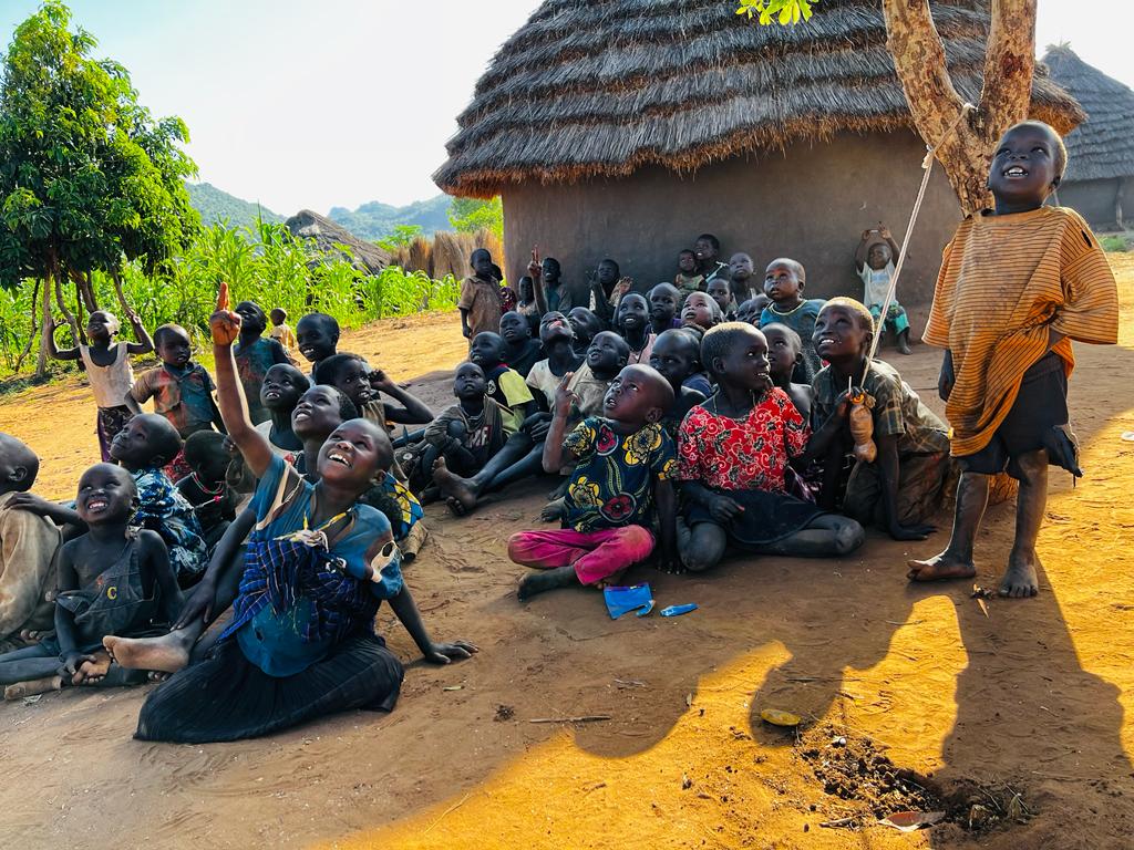 Children gathered outside a traditional thatched-roof house in a rural setting in Karamoja region engaging in an outdoor activity while — Uganda